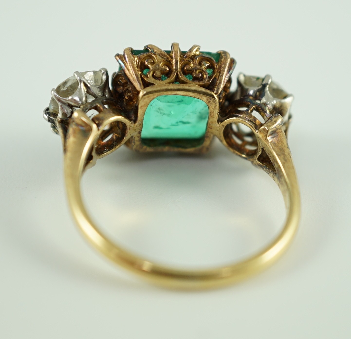 An early 20th century 18ct gold, square cut single stone emerald and two stone cushion cut diamond set dress ring